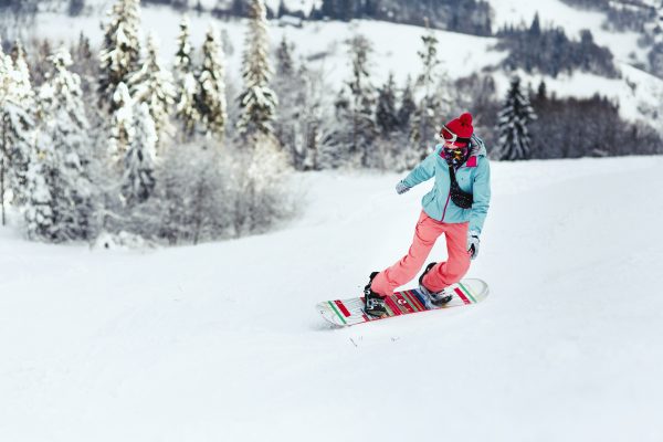 woman in ski suit looks over her shoulder going down the hill on her snowboard scaled